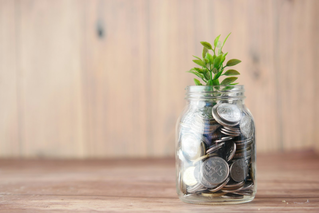 A glass jar of coins beside a fresh green leaf
